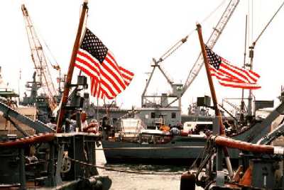 Two ocean minesweepers lie tied up in the foreground as a third ocean minesweeper is moved in alongside them. The three U.S. Navy ocean minesweepers and a mine countermeasures ship are being loaded aboard the SUPER SERVANT 3 for transportation to the Persian Gulf, where they will support U.S. forces sent to the region in reaction to Iraq`s invasion of Kuwait. The nuclear-powered aircraft carrier USS ENTERPRISE (CVN-65) is in the background.<br>
Location: NAS NORFOLK, VIRGINIA (VA) UNITED STATES OF AMERICA (USA)<br>
Date Shot: 19 AUG 1990